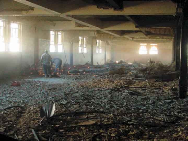 Fire aftermath interior with workers clearing debris and smoldering remains