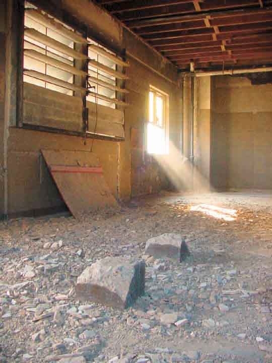 Debris-filled building interior with sunlight streaming through damaged windows